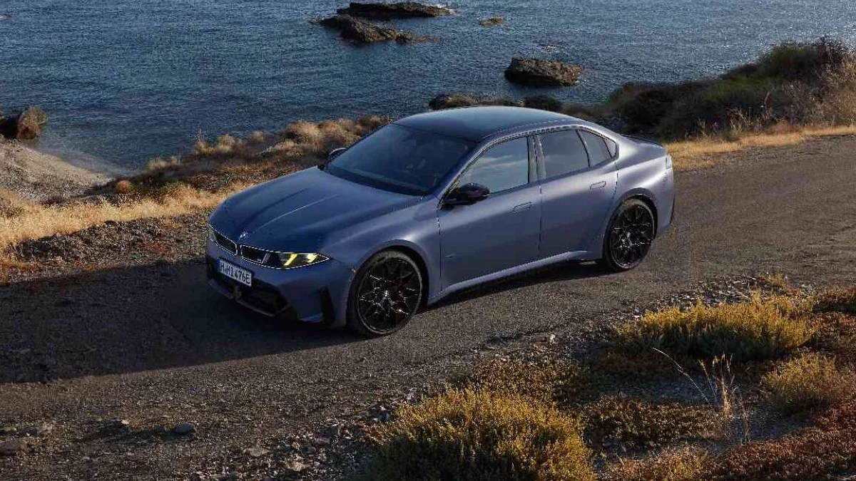 Yeni BMW 3 Serisi M350 xDrive'ın sarı M ışıklı ön farları ve Neue Klasse tasarımıyla sahil yolunda çekilmiş resmî basın fotoğrafı