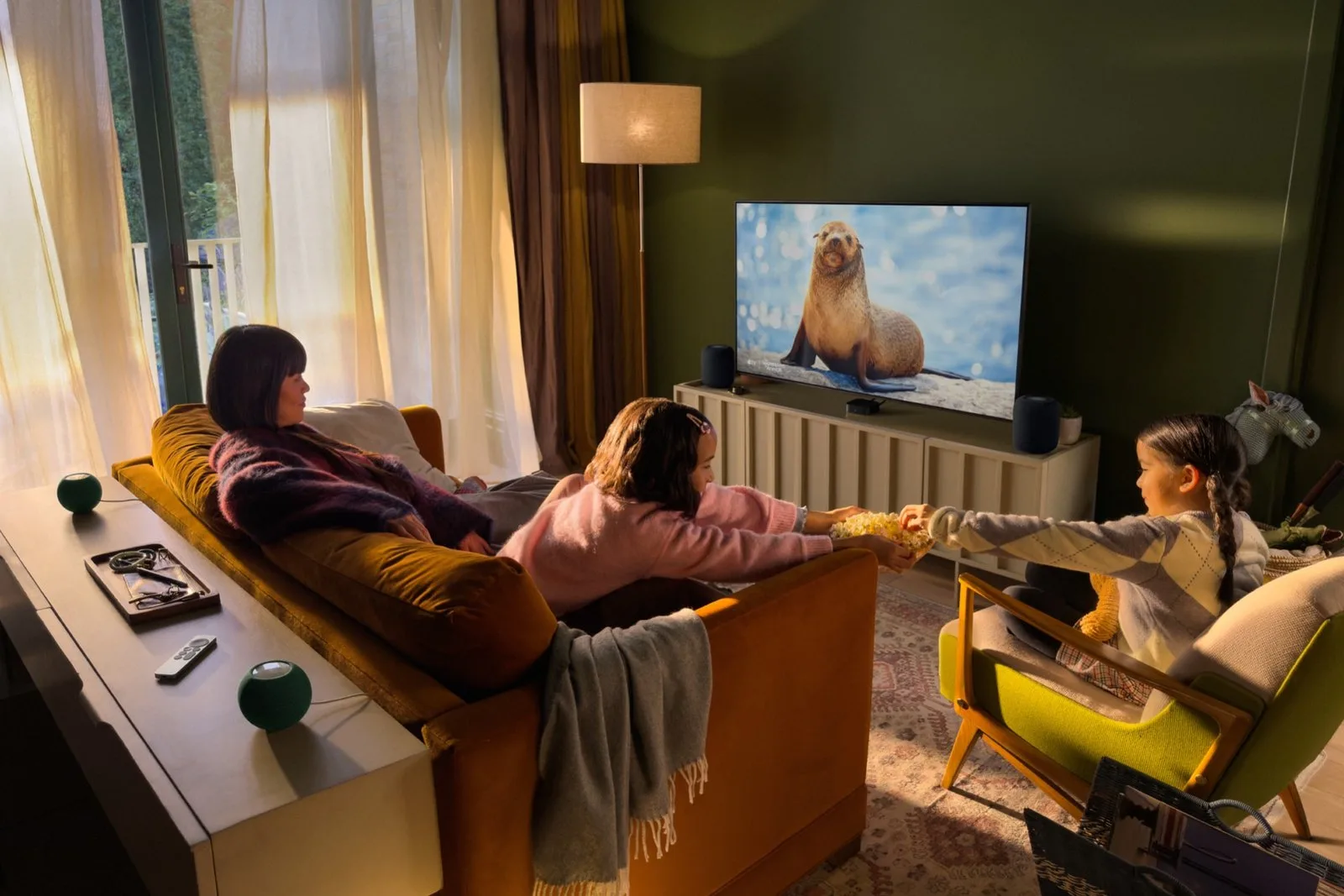 Oturma odasında televizyonun iki yanında ve kanepenin arkasında HomePod mini 2 hoparlörleriyle dört hoparlörlü ev sineması