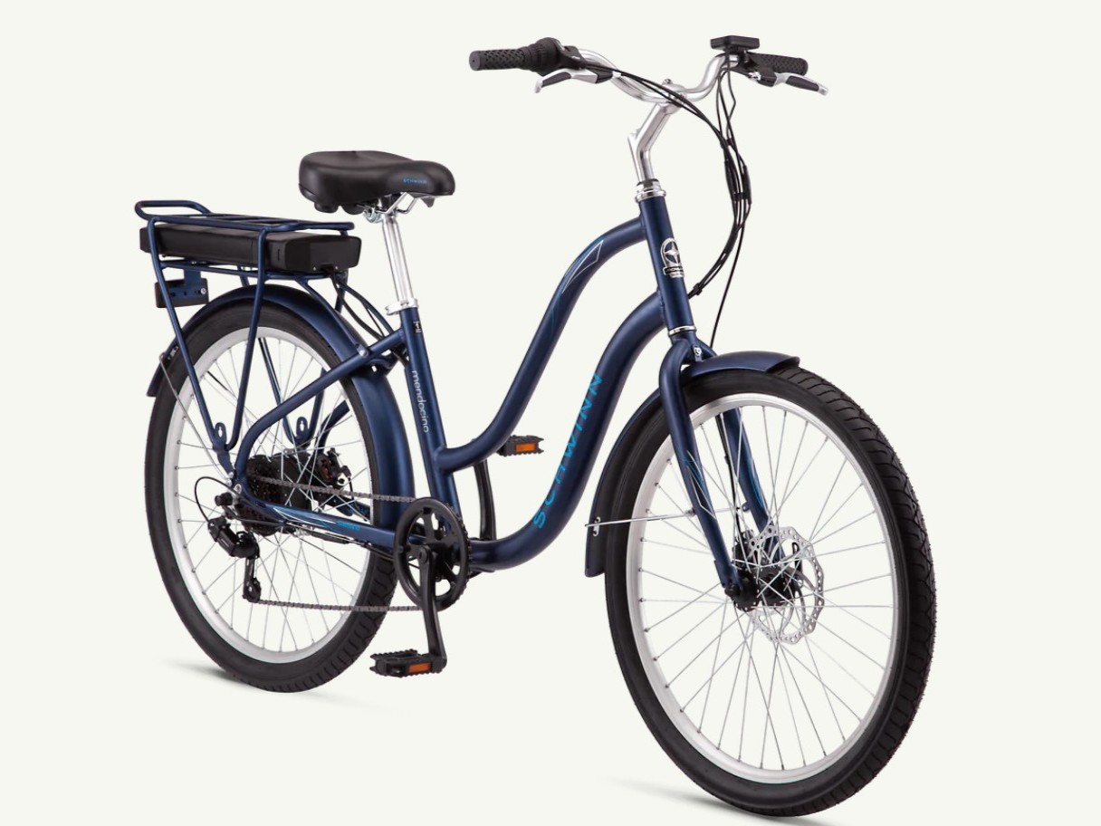Schwinn Mendocino Hybrid Cruiser e-bike on an urban path with greenery and blue sky, showcasing its sleek design and features.